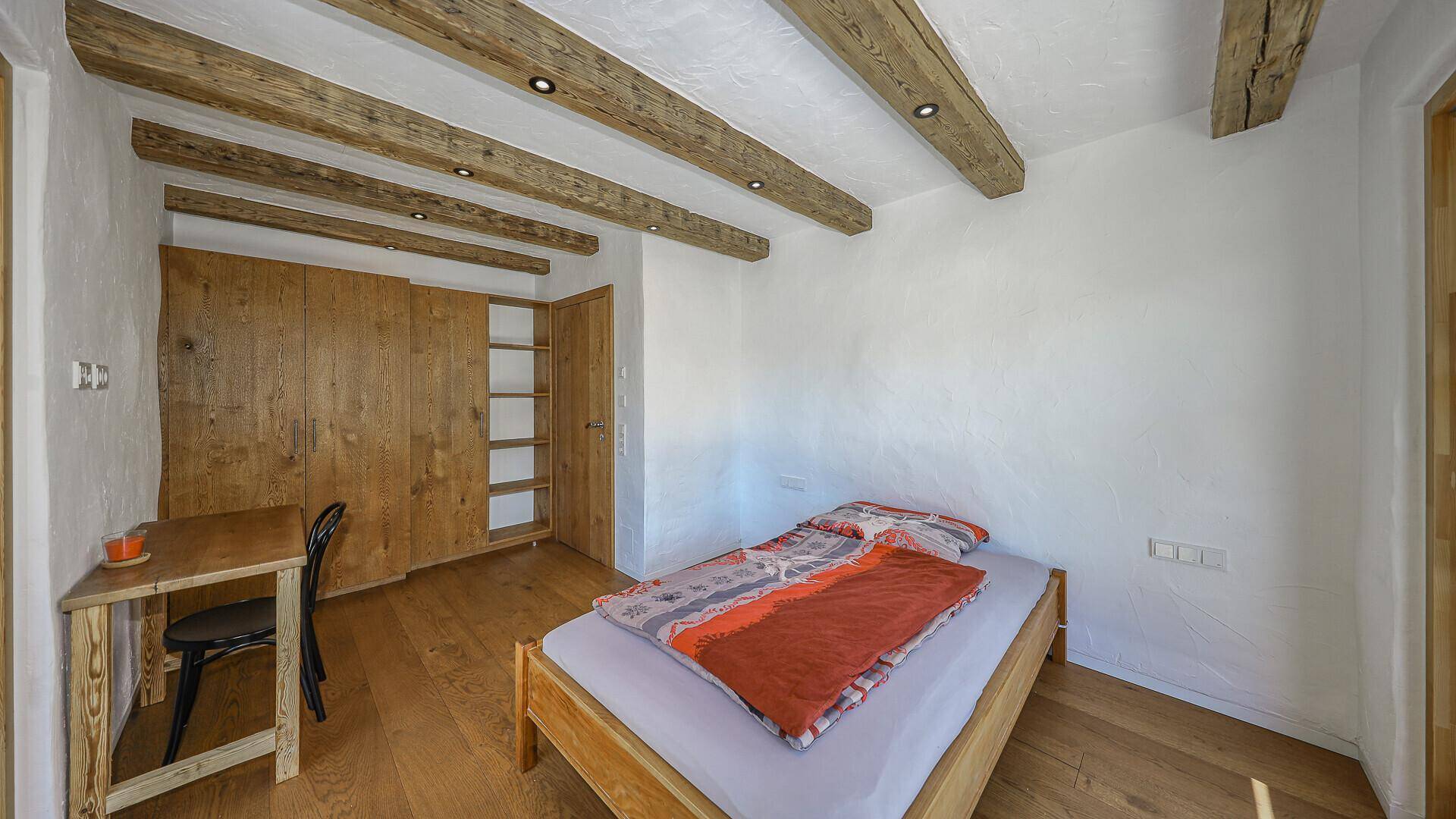Gemütliches Schlafzimmer mit Holzbalken, Parkettboden und integriertem Holzschrank.