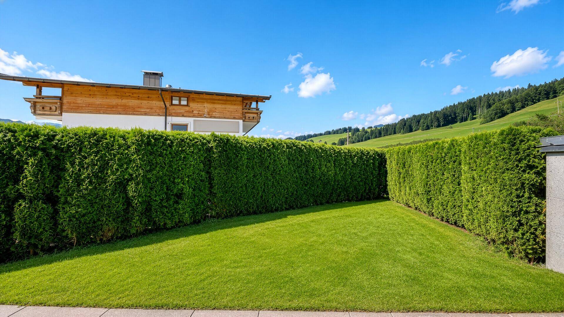 Weitläufiger Rasenbereich mit hoher Hecke und Blick auf die umliegende Landschaft.