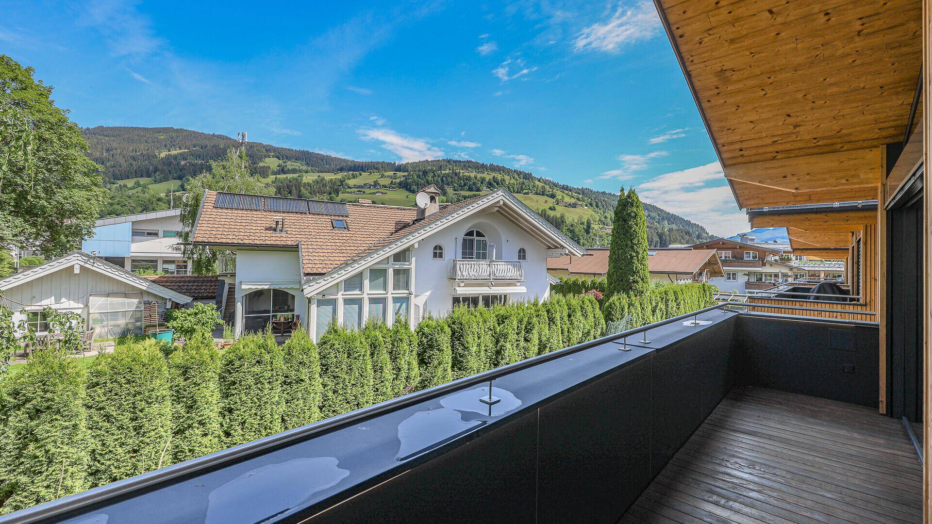 Geräumiger Balkon mit Holzboden und Blick auf die grüne Umgebung und die Berge.