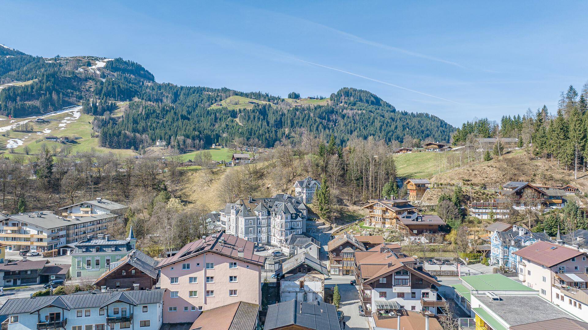 Weitläufige Luftaufnahme der Stadt mit ihren Gebäuden und der beeindruckenden Bergkulisse im Frühling.