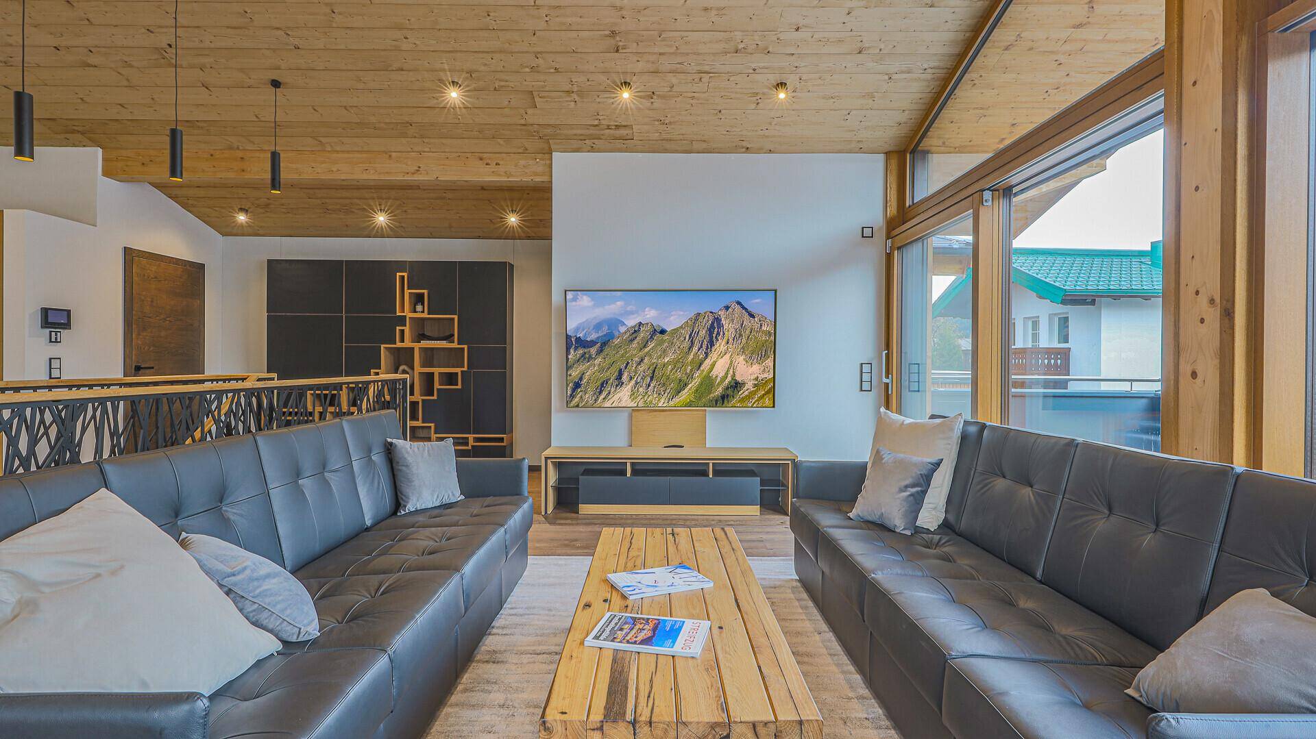 Gemütliches Wohnzimmer mit bequemen Sofas, Holztisch und großem Fernseher mit Bergblick.