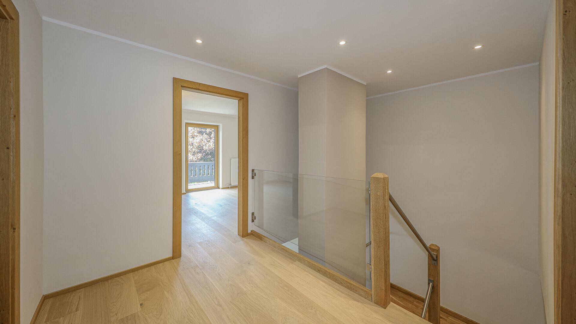 Heller Flur mit Holzboden, Glasgeländer und Zugang zu einem Raum mit Balkon.