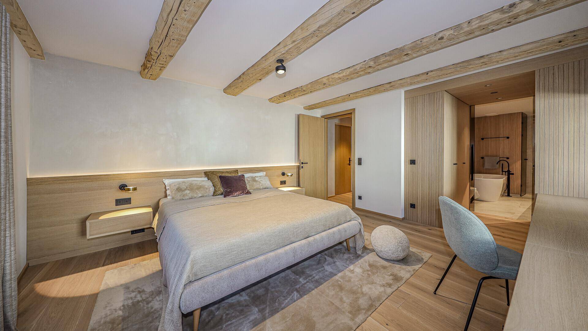 Helles Schlafzimmer mit Holzbalken, Holzboden und direktem Zugang zum Badezimmer.