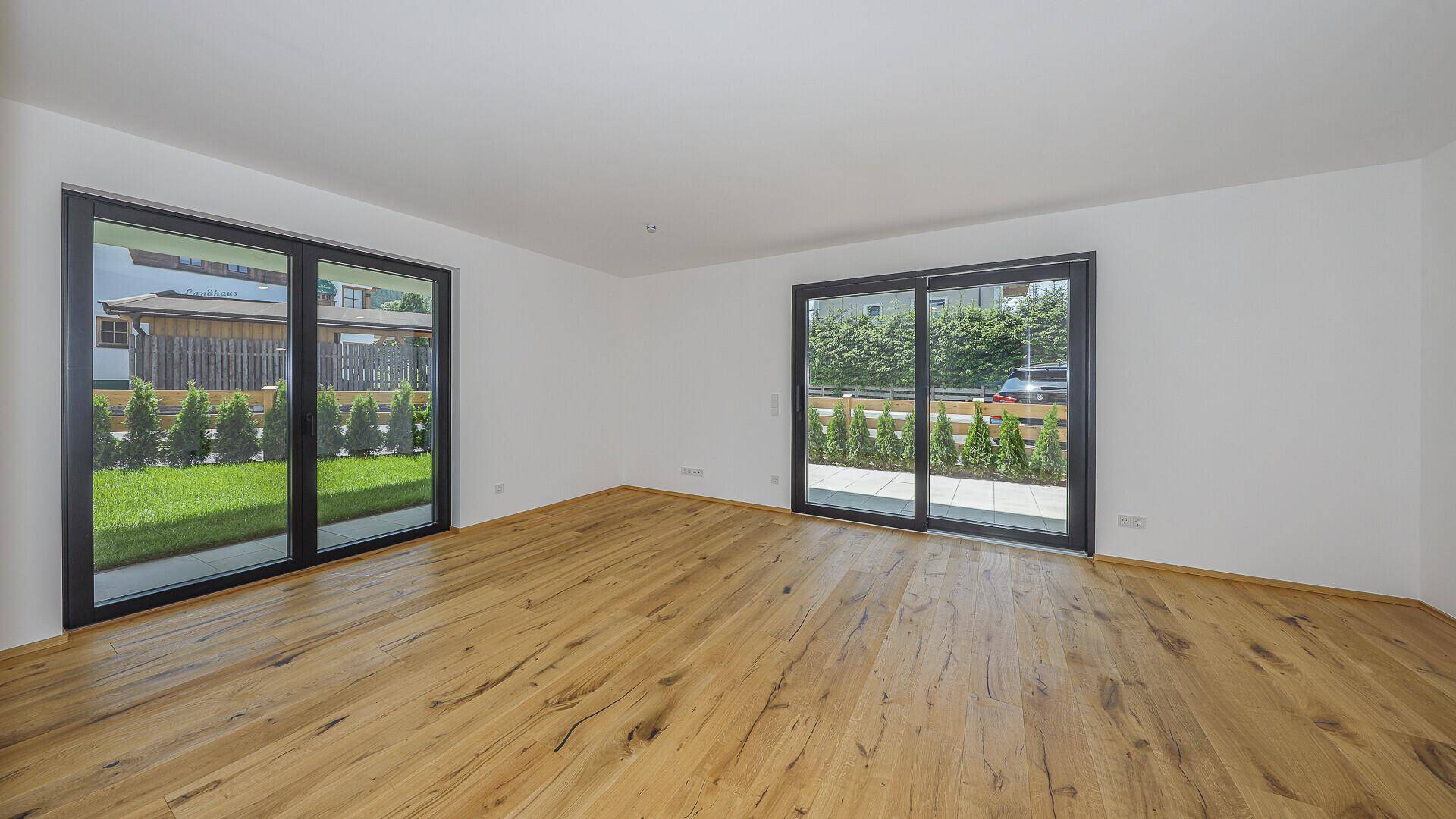 Heller, leerer Wohnbereich mit Holzboden und großen Schiebetüren zum Garten.