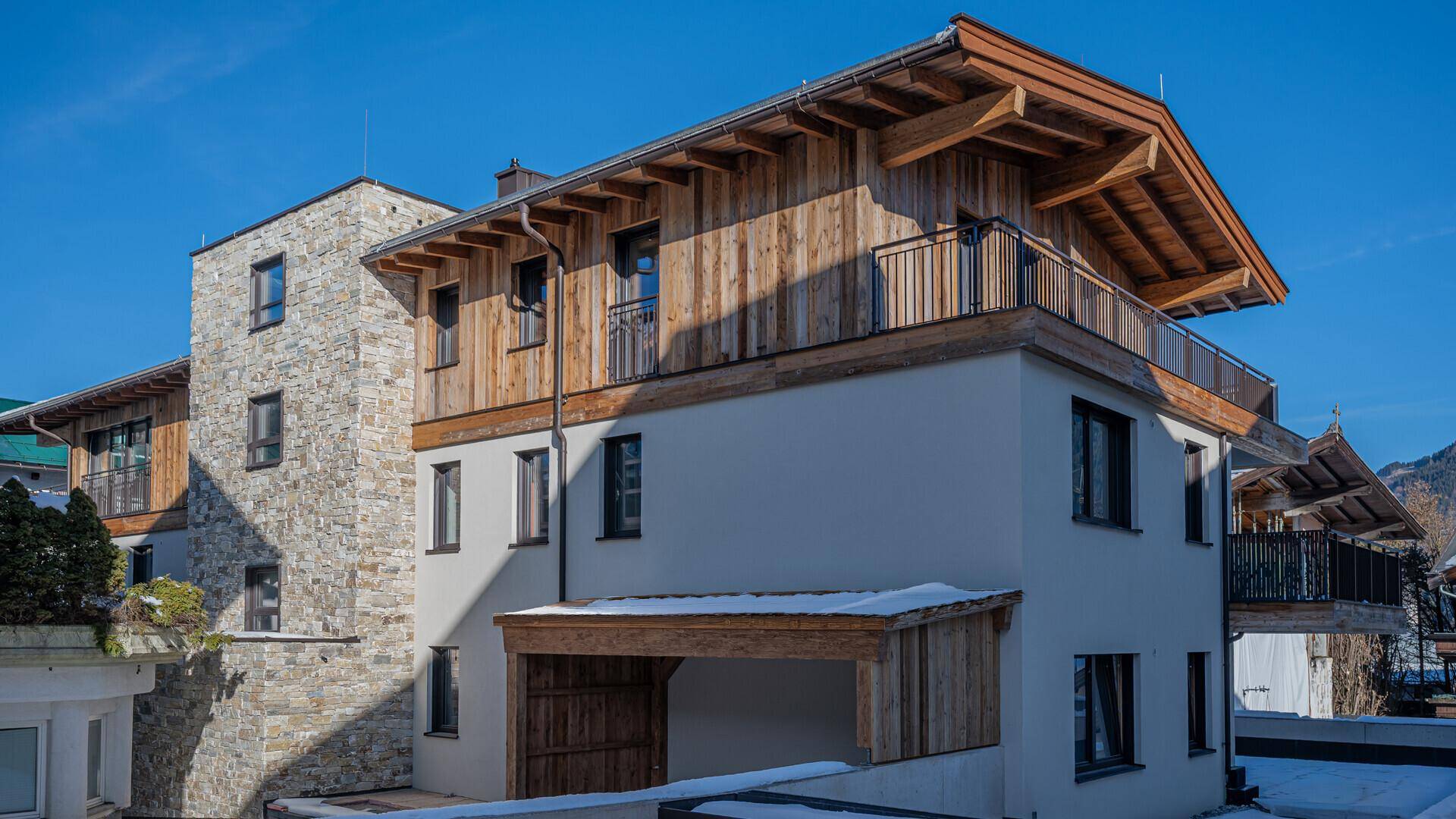 Moderne Fassade eines Neubaus im alpinen Stil mit Holzelementen und Steinverkleidung.
