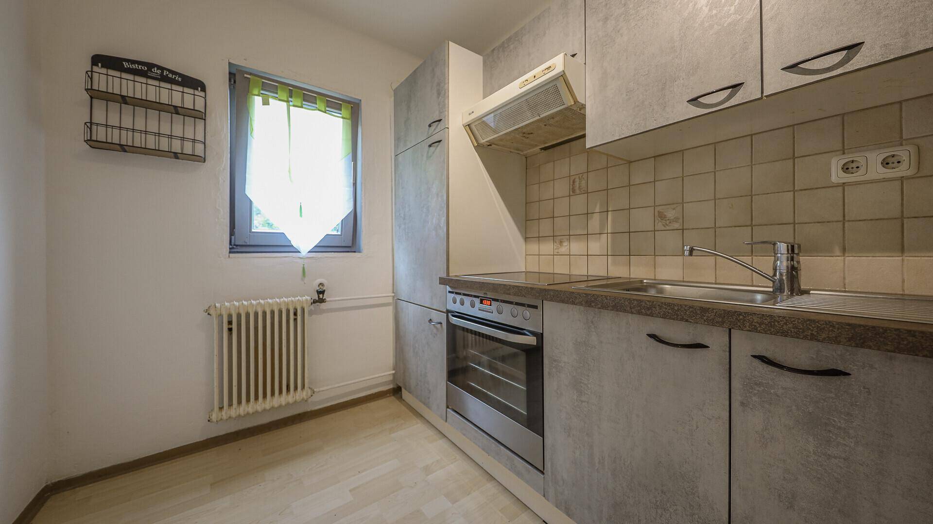 Funktionale Küche mit grauen Schränken, Einbauherd, Spüle und Fenster.