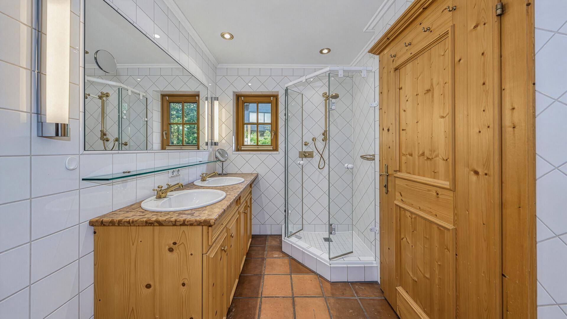 Traditionelles Badezimmer mit Doppelwaschbecken, Duschkabine und Holzmöbeln.