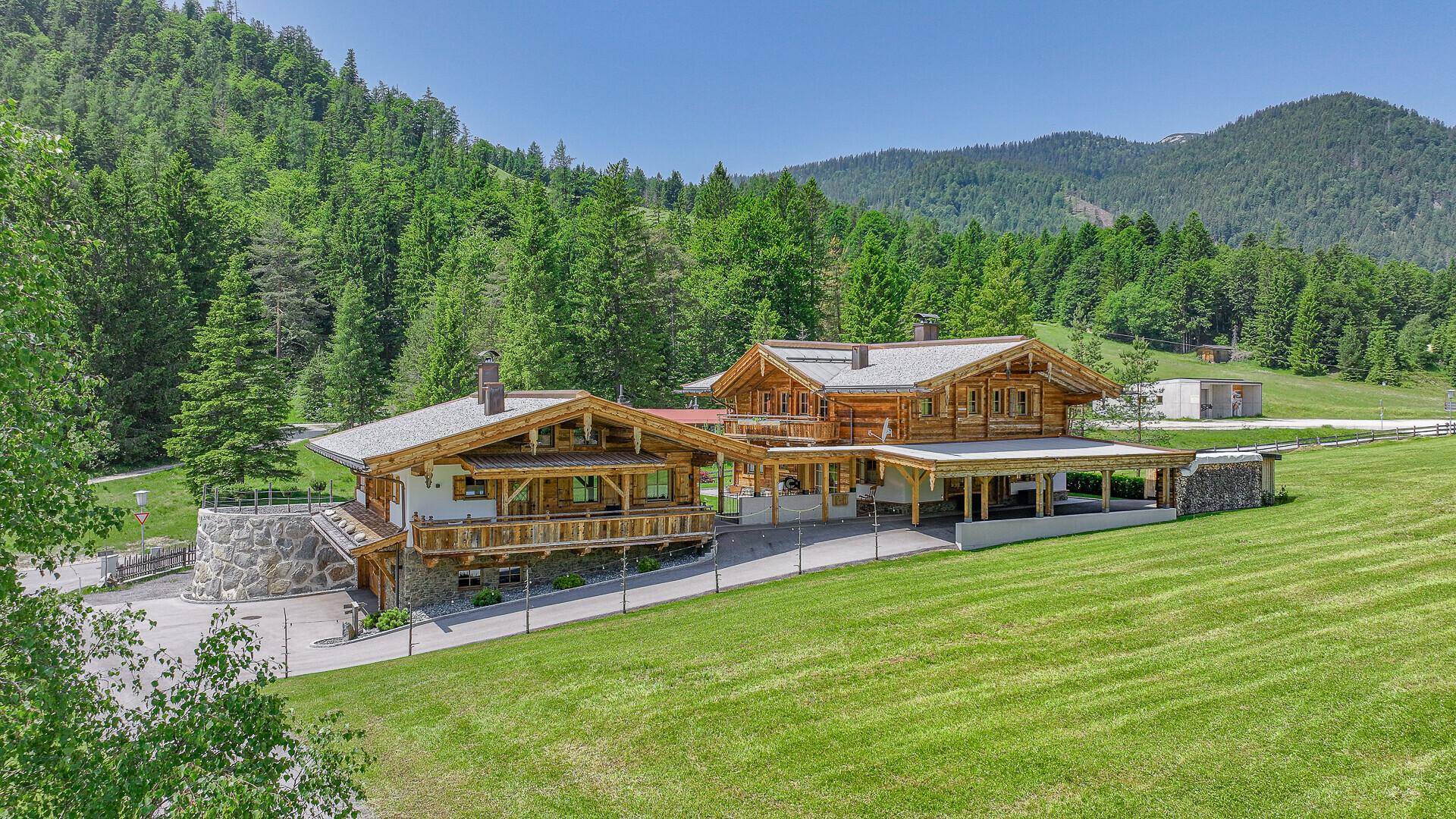 Luftaufnahme von zwei Chalets mit Holzbalkonen und weitläufigen Grünflächen, umgeben von Wald und Bergen.