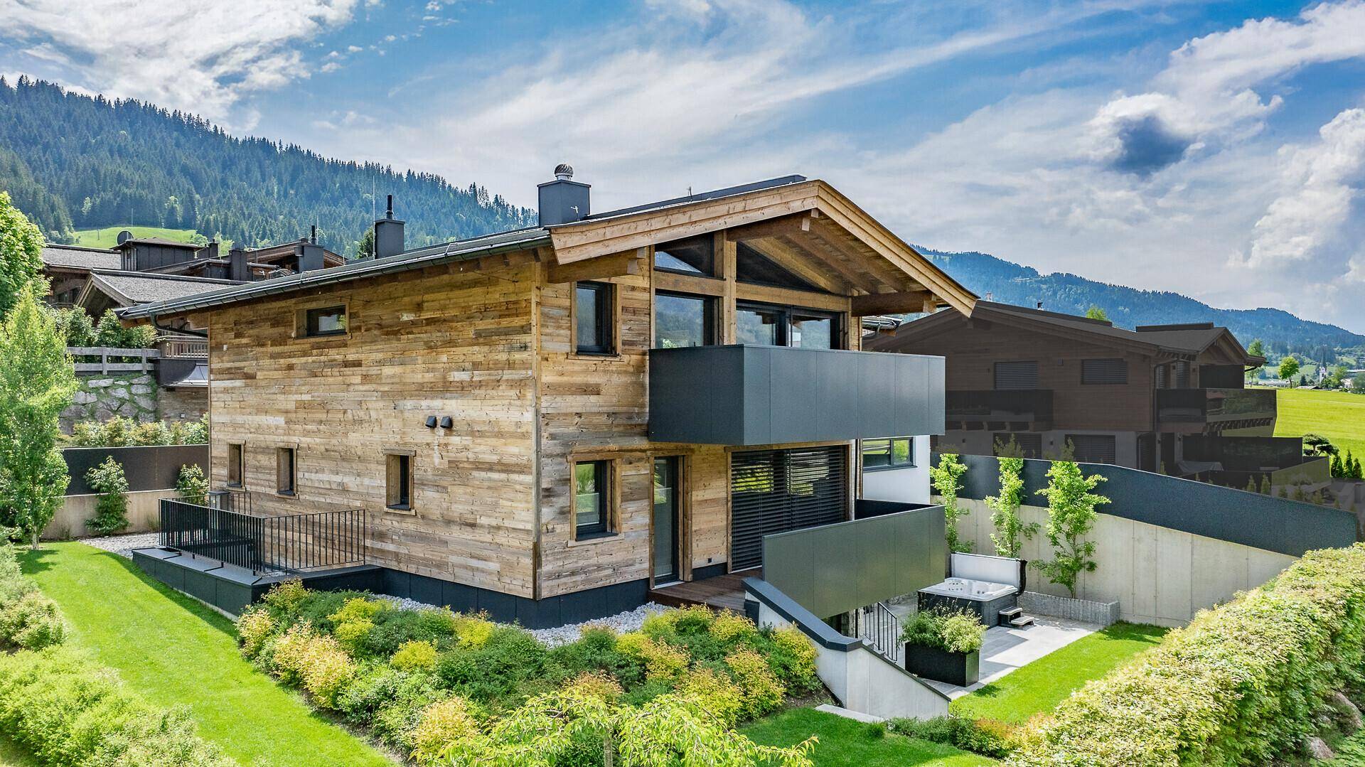 Rückansicht des modernen Chalets mit Holzfassade, Balkonen und gepflegtem Gartenbereich.