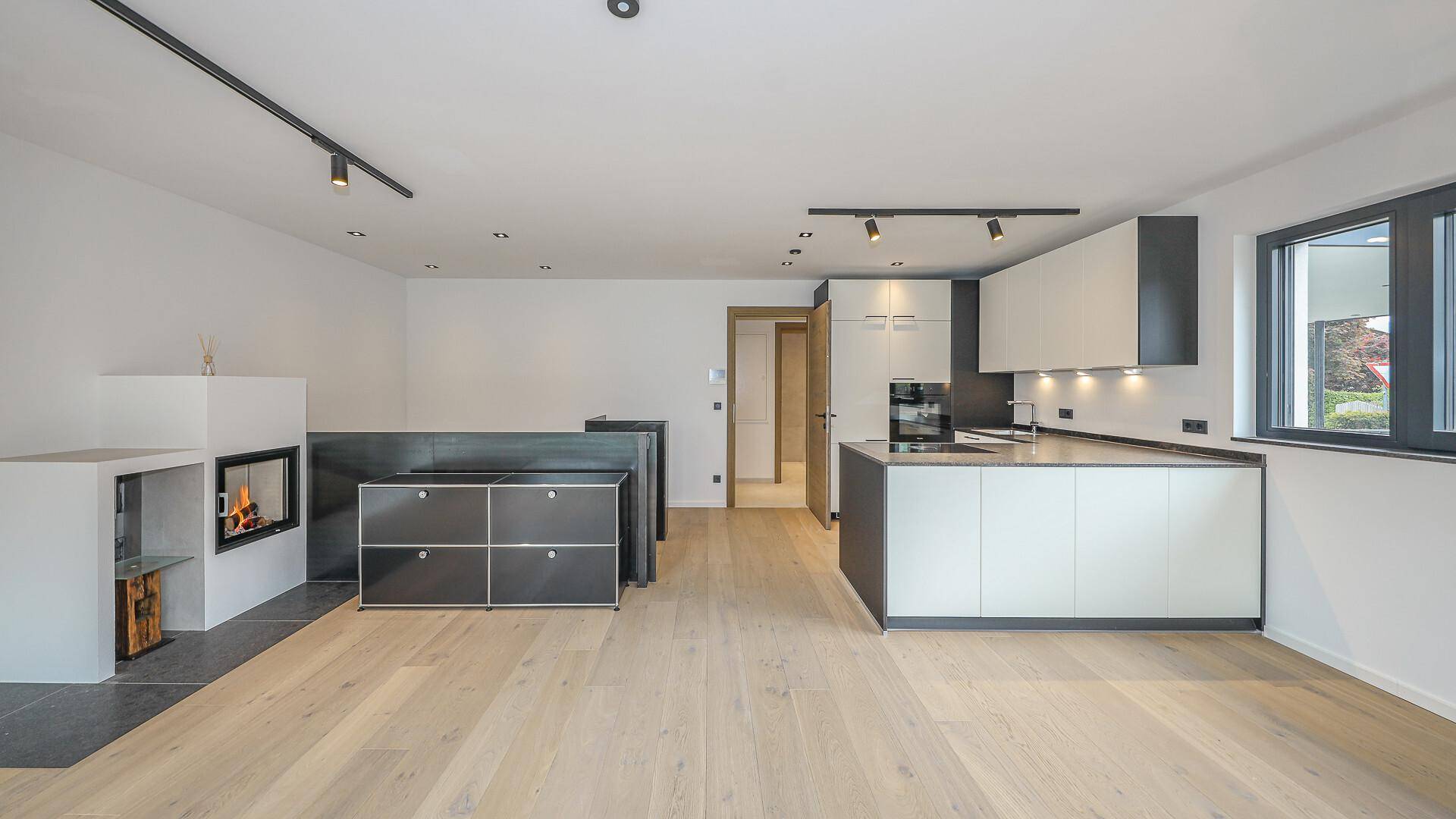 Heller offener Wohnbereich mit moderner Küche, Kamin und Holzboden.