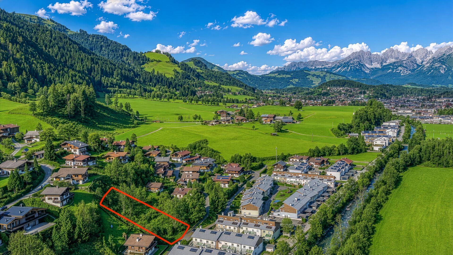 Luftaufnahme eines Grundstücks, rot umrandet, in einem grünen Tal mit Bergblick.