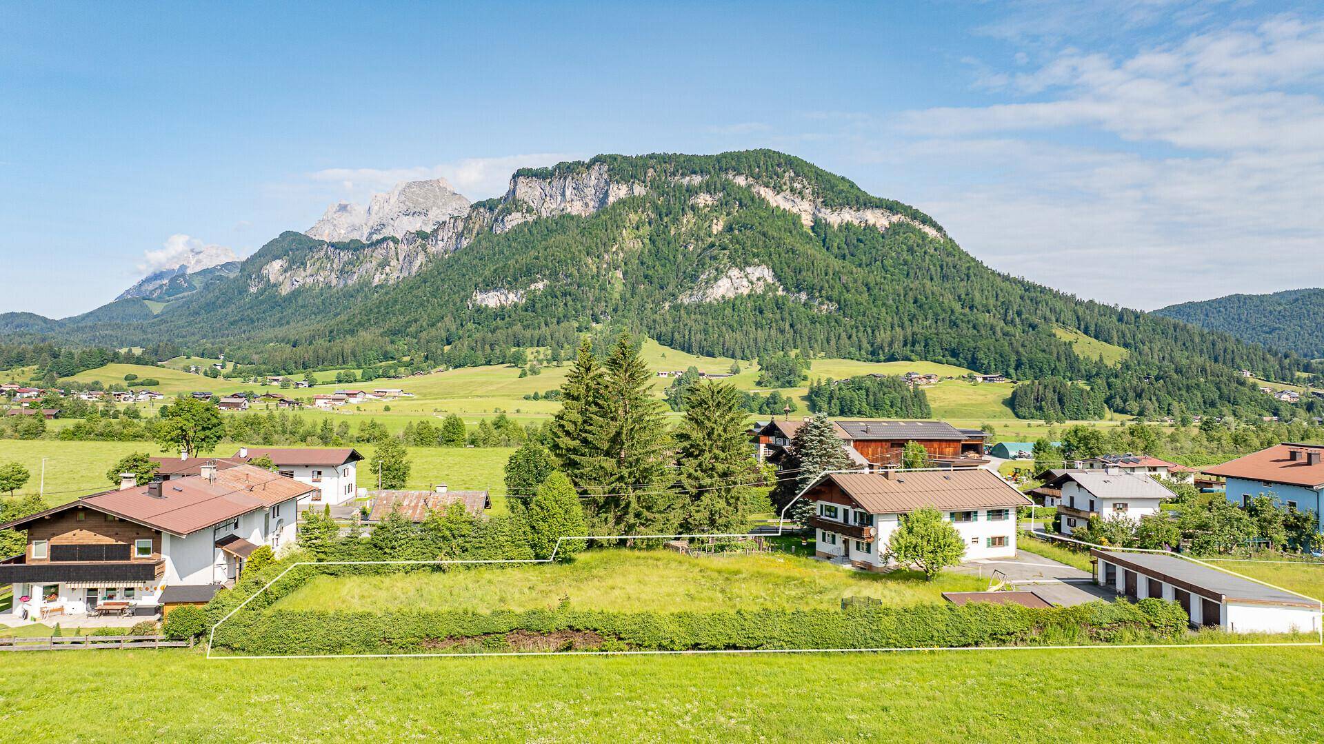 Übersicht des Baugrundstücks mit angrenzenden Häusern und der malerischen Bergkulisse.