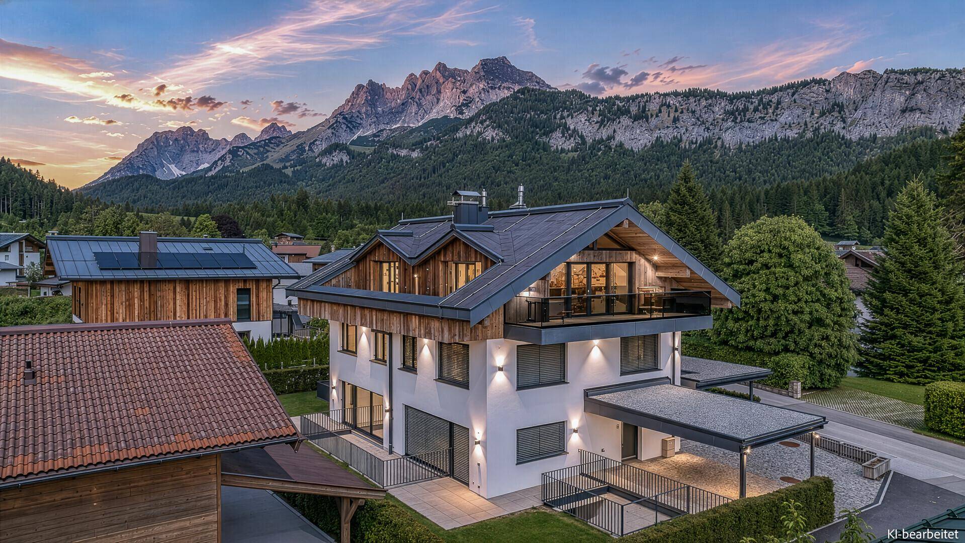 Modernes Haus in alpiner Landschaft bei Sonnenuntergang mit beleuchteter Fassade und Bergblick.