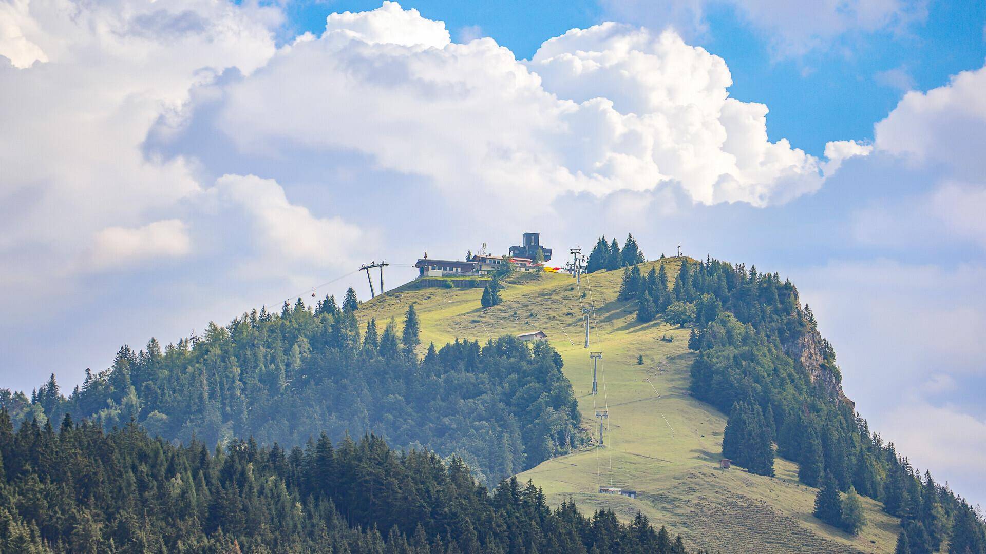 Grüner Berg mit Seilbahnstation und bewölktem Himmel.