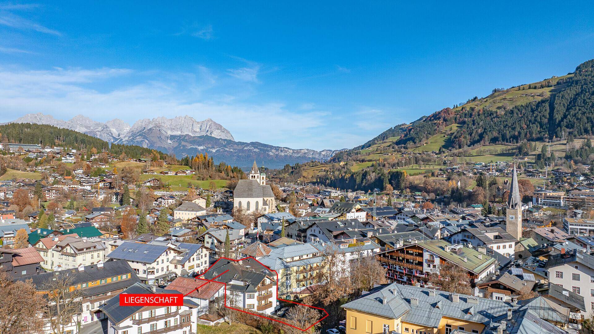 Panoramablick auf die Stadt mit Kirche und umliegenden Bergen unter blauem Himmel.