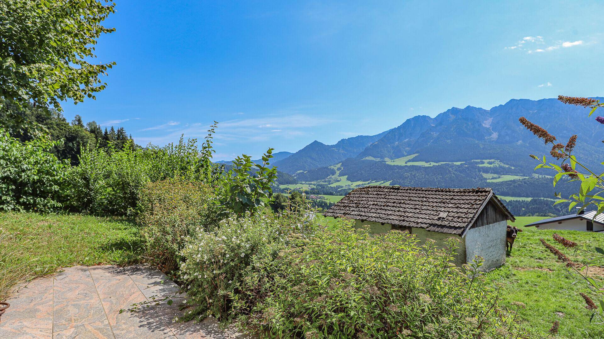 Rustikales Nebengebäude mit Ziegeldach, umgeben von üppigem Grün und malerischem Bergblick.