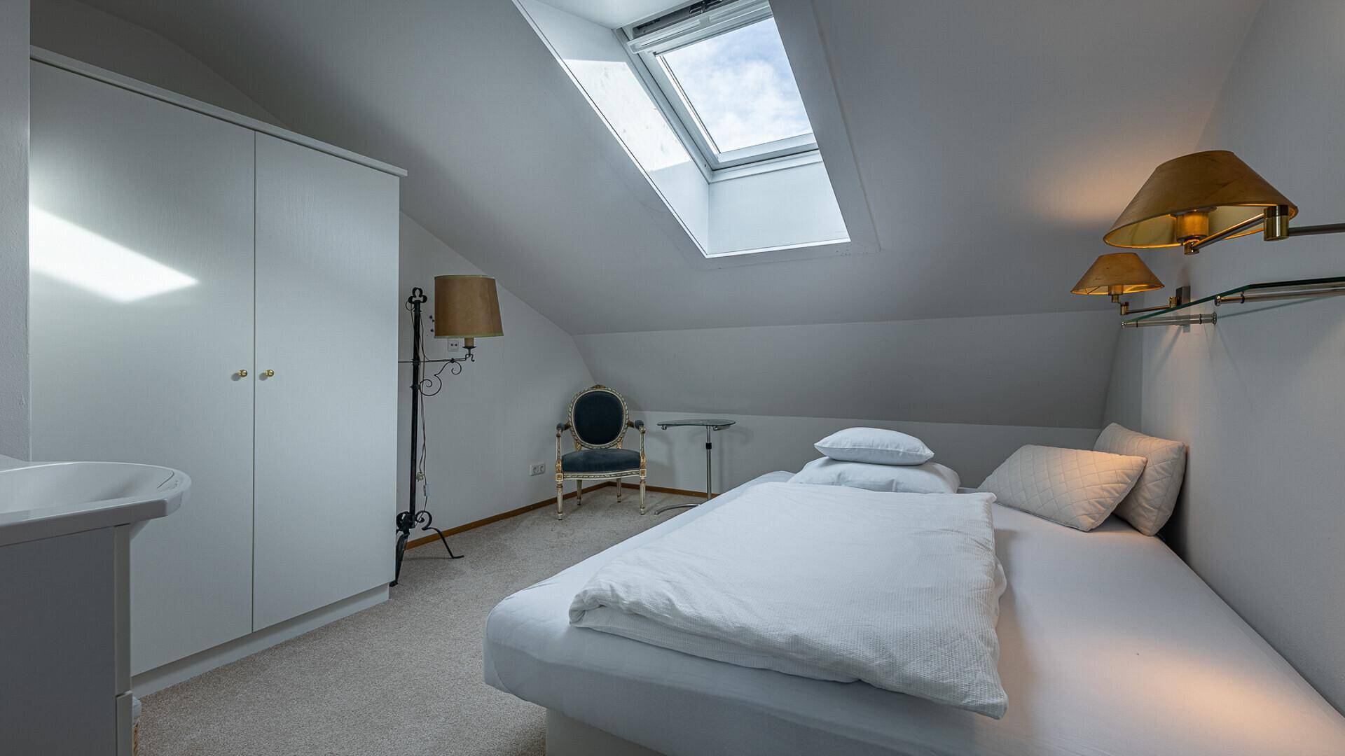 Gemütliches Dachgeschoss-Schlafzimmer mit Einzelbett, Dachfenster und integrierten Schränken.