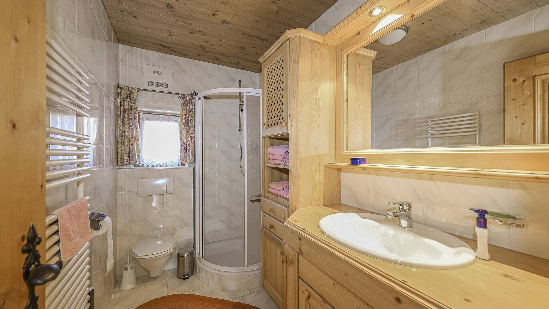 Helles Badezimmer mit Dusche, Waschtisch und beheiztem Handtuchhalter.