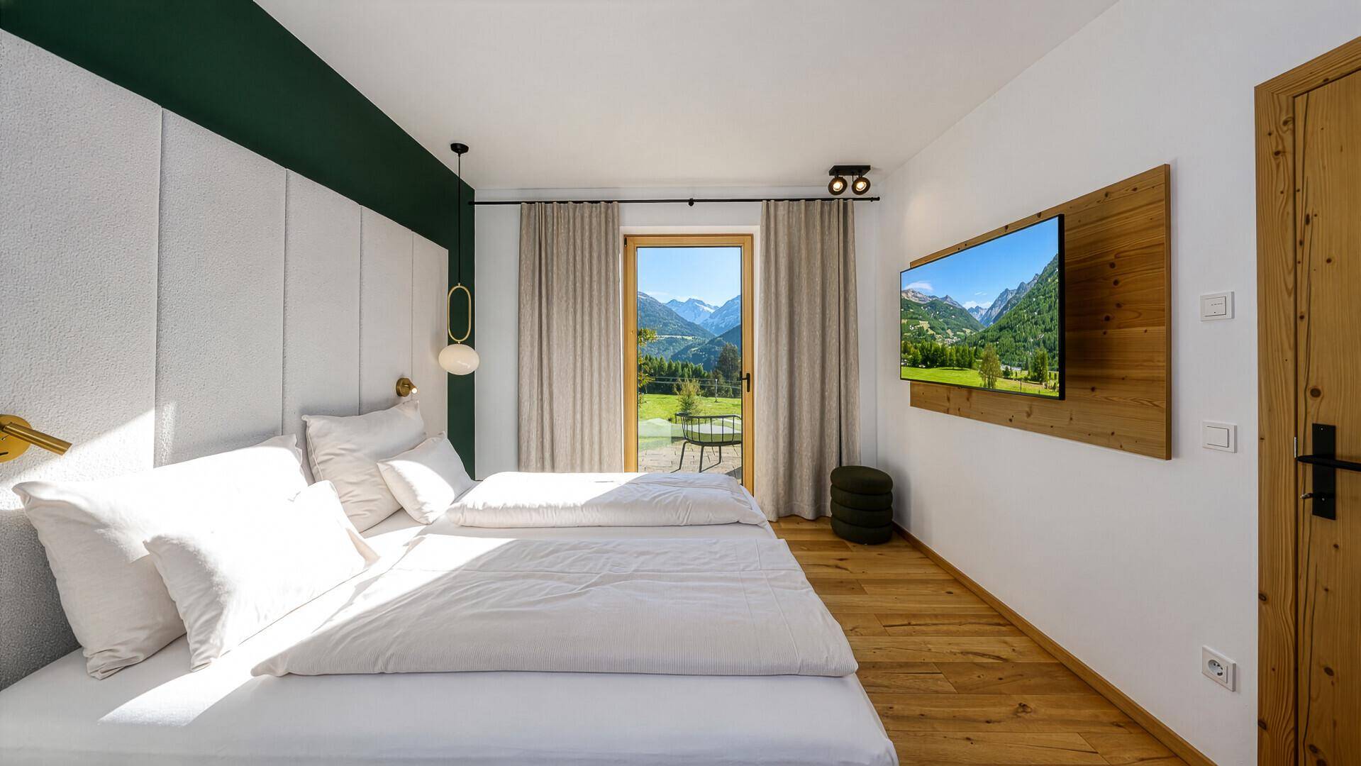 Helles Schlafzimmer mit Doppelbett, Holzboden und direktem Zugang zu einem Balkon mit Bergblick.