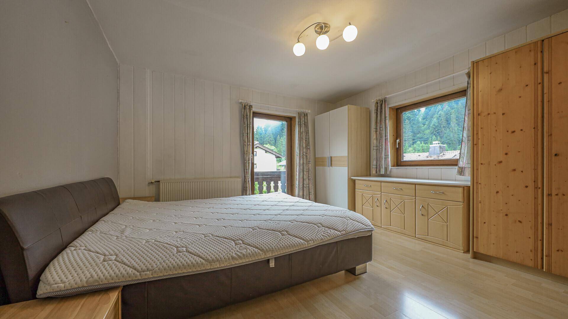 Helles Schlafzimmer mit Holzboden, Kleiderschrank und Zugang zum Balkon.