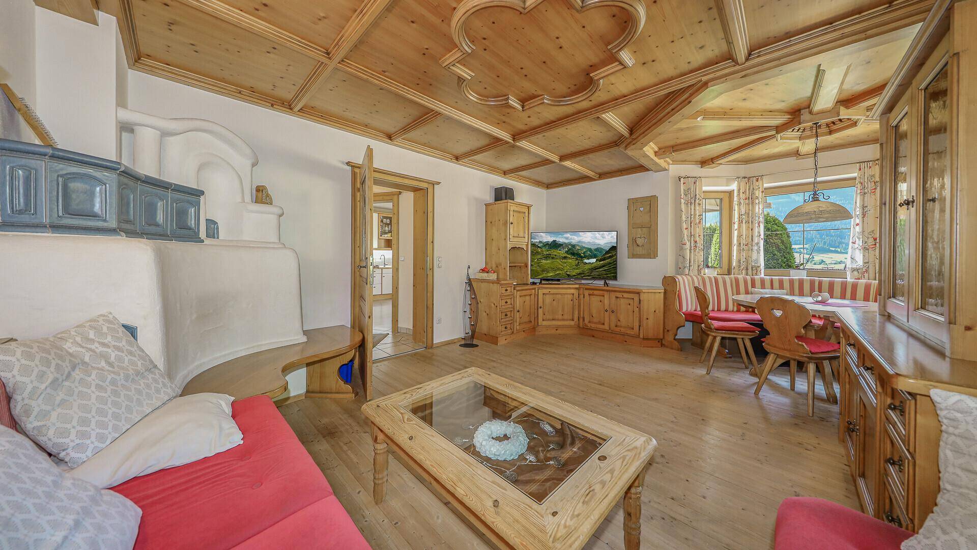 Gemütlicher Wohn-Essbereich im alpinen Stil mit Kachelofen, Holzbalkendecke und traditionellen Möbeln.