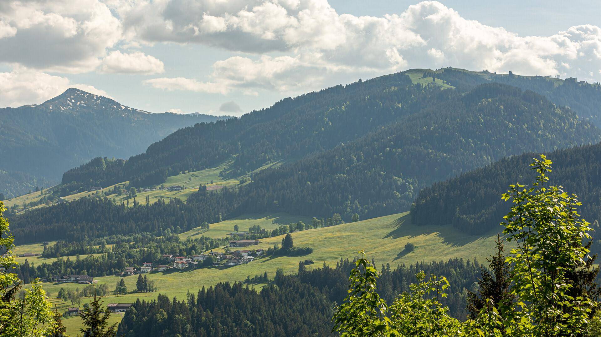Panoramablick auf eine malerische Berglandschaft mit dichten Wäldern und kleinen Siedlungen.