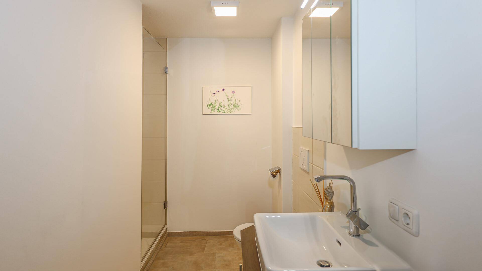 Modernes Badezimmer mit Dusche, Waschbecken und Spiegel, in hellen Farbtönen gehalten.