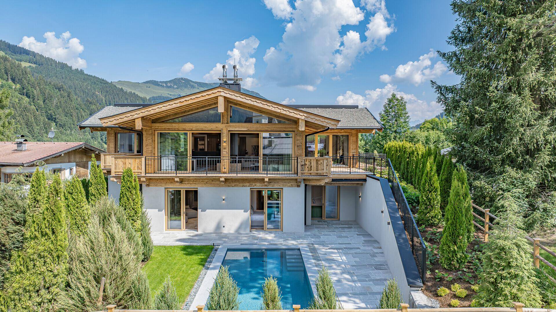 Luxuriöses Chalet mit Holzfassade, großem Poolbereich und üppiger Bepflanzung in den Bergen.