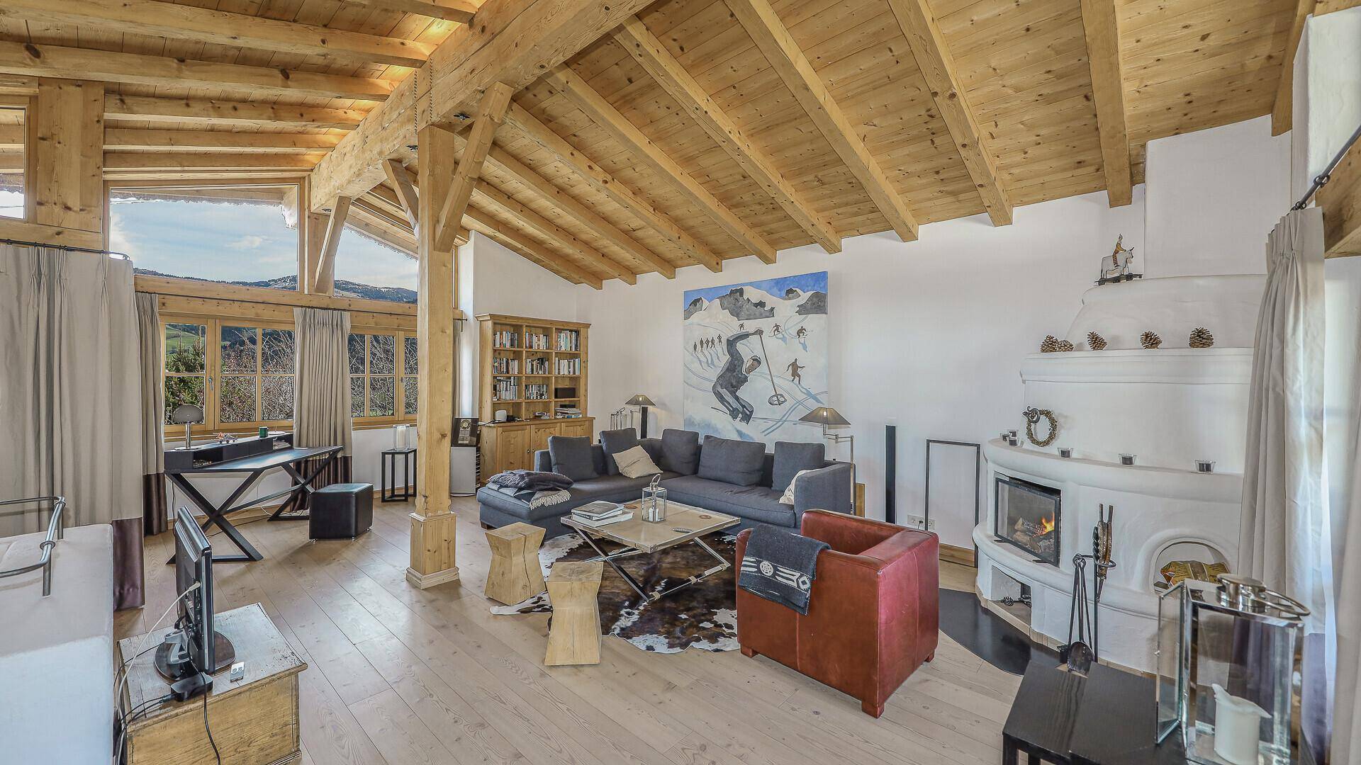 Geräumiger Wohnbereich mit Kachelofen, Holzbalkendecke und Zugang zum Balkon.