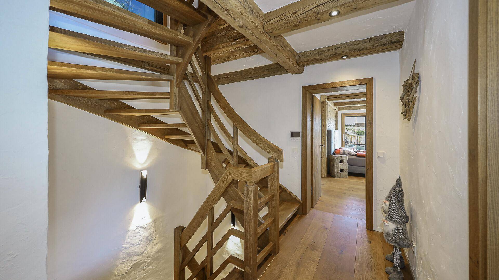 Heller Flur mit Holztreppe, Holzbalken und Parkettboden, der zu den Wohnbereichen führt.