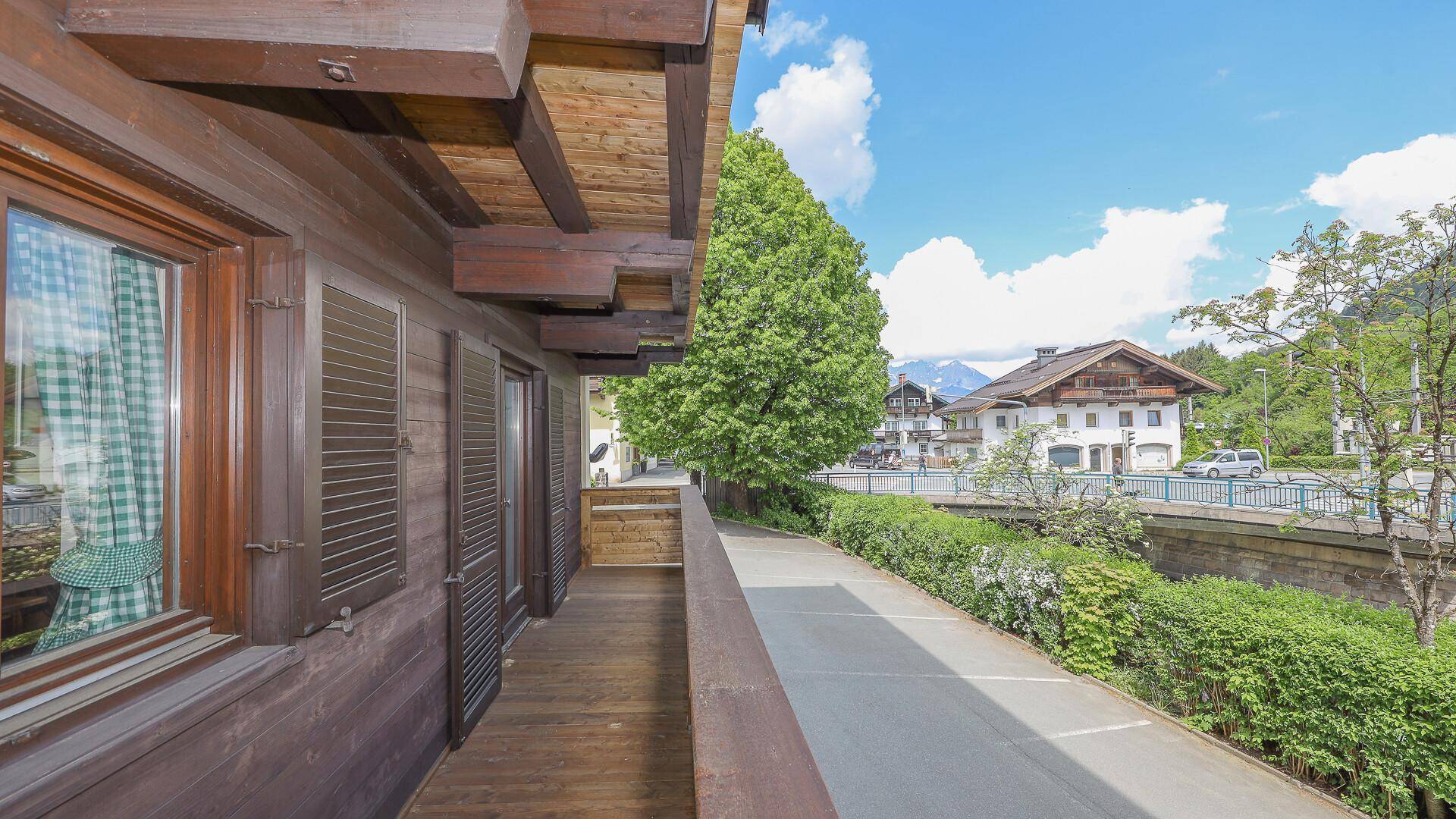 Langer Holzbalkon mit Blick auf die Straße und umliegende Gebäude in alpiner Umgebung.