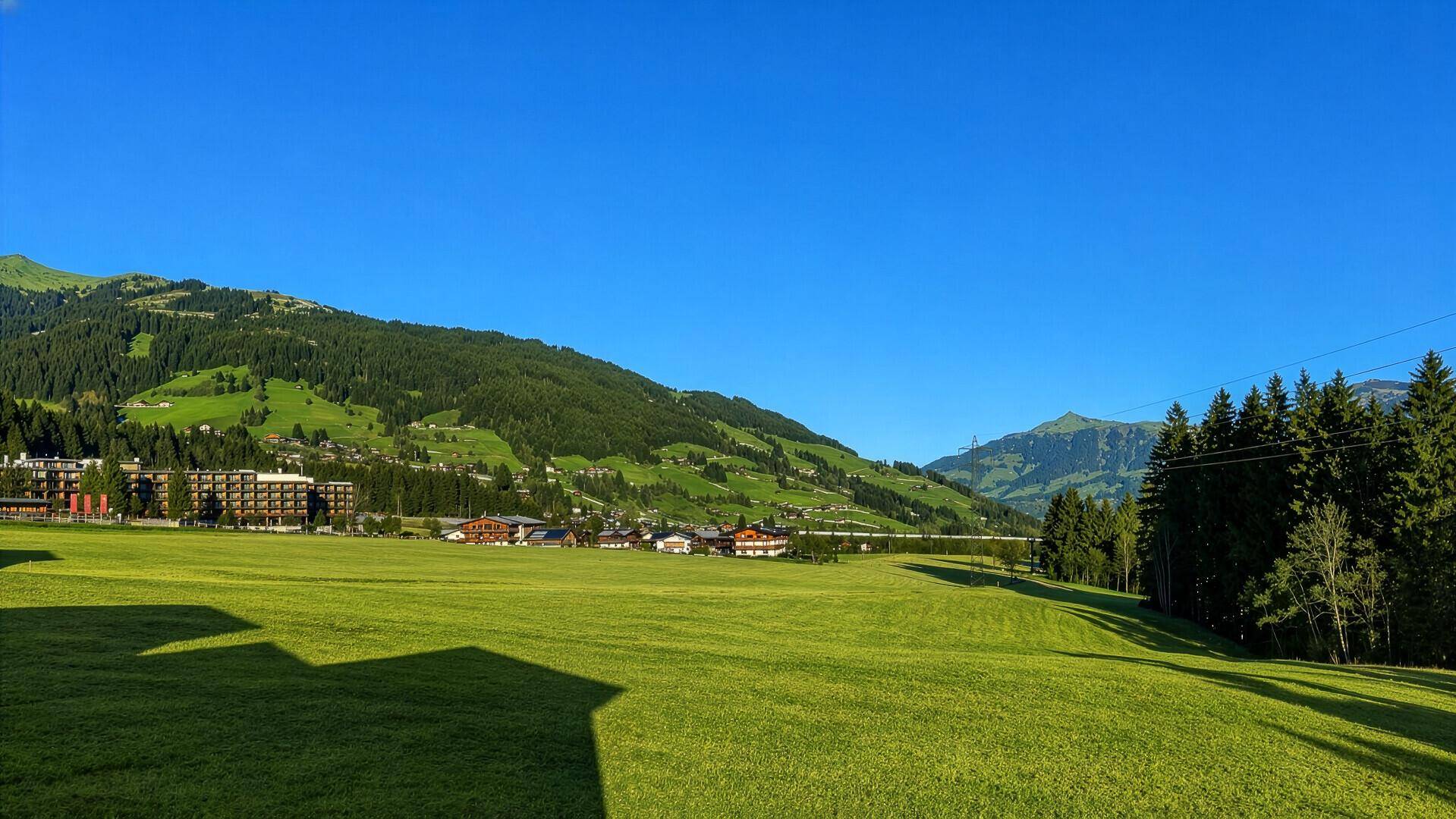 Weite grüne Wiesen mit majestätischen Bergen im Hintergrund unter blauem Himmel.