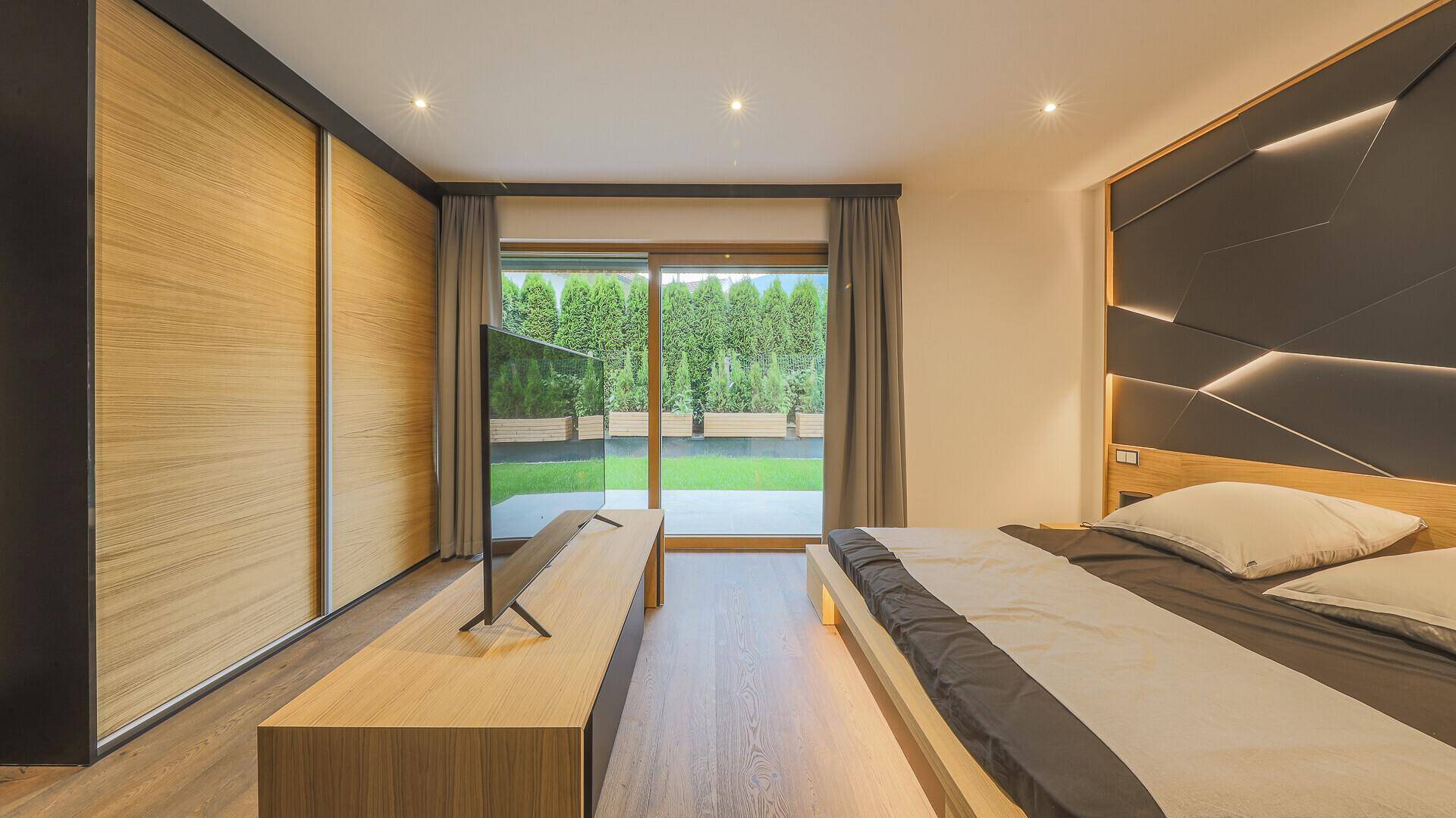 Modernes Schlafzimmer mit Holzboden, Einbauschränken und Zugang zu einem Gartenbereich.