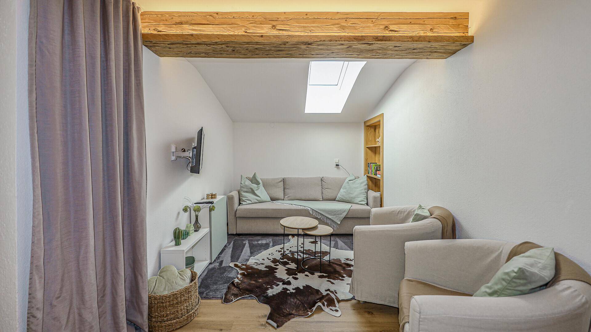 Heller Wohnbereich mit bequemer Couch, rustikalem Teppich und einem Dachfenster für viel Tageslicht.