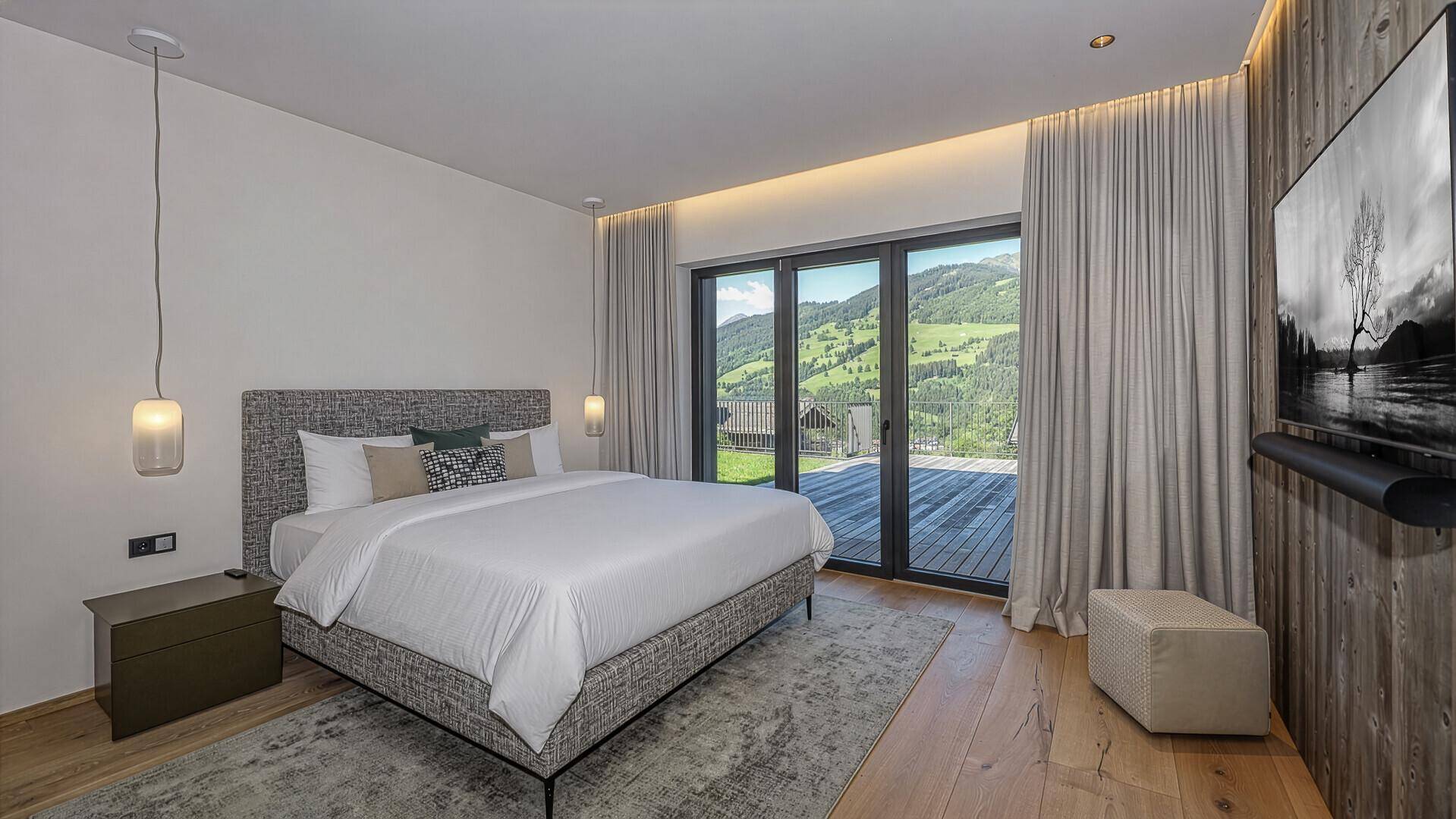 Helles Schlafzimmer mit Holzwand, großem Bett und Zugang zu einer Terrasse mit Bergblick.