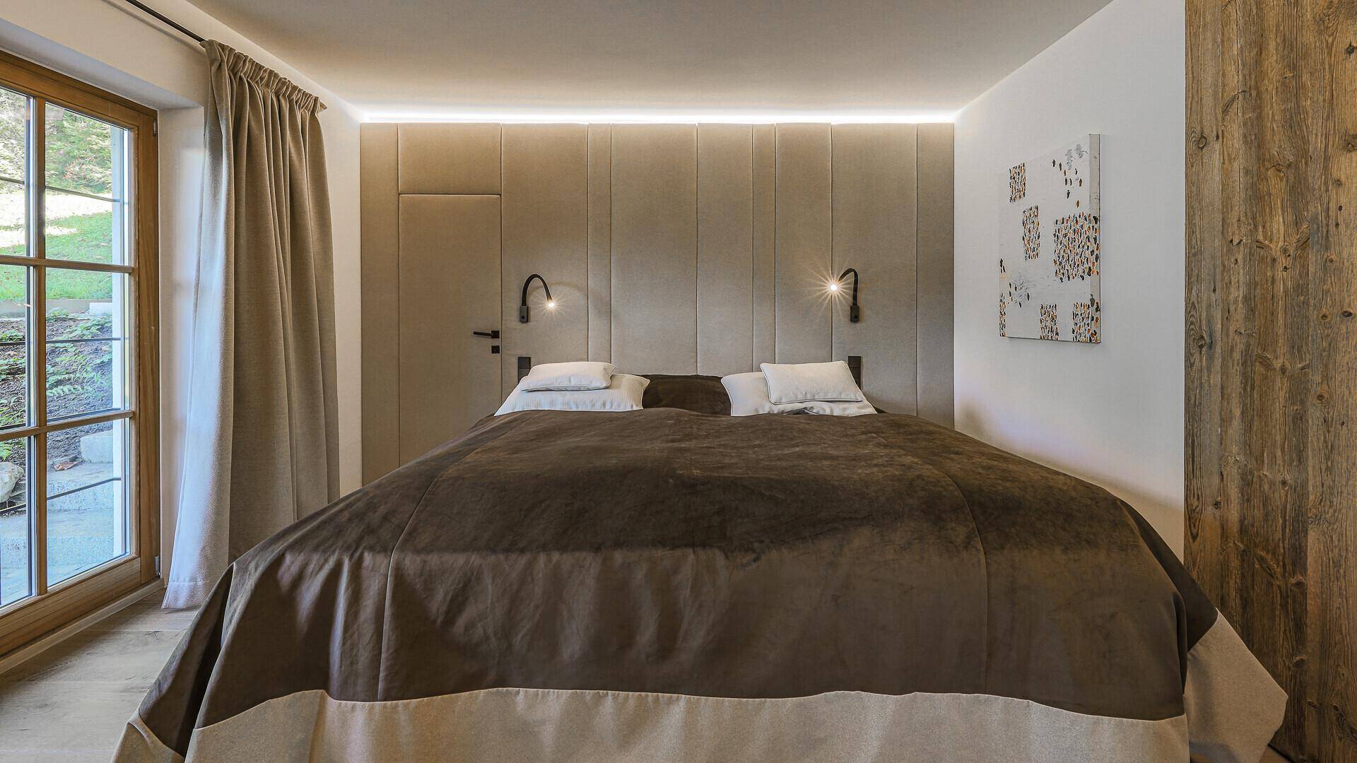 Gemütliches Schlafzimmer mit großem Doppelbett, gepolstertem Kopfteil und Zugang zum Garten.