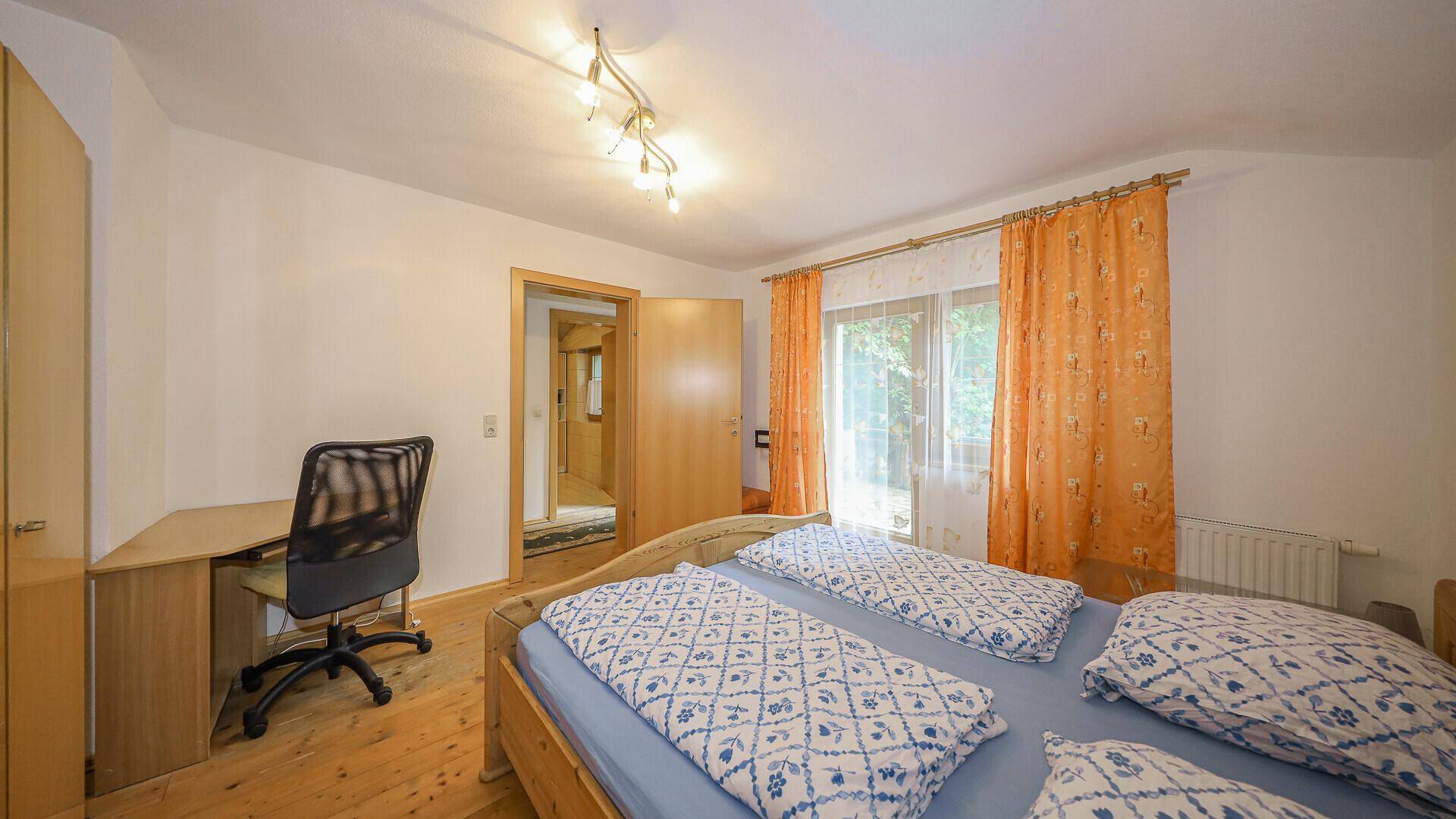 Schlafzimmer mit Arbeitsbereich, Holzdielenboden und Zugang zu einem Flur.