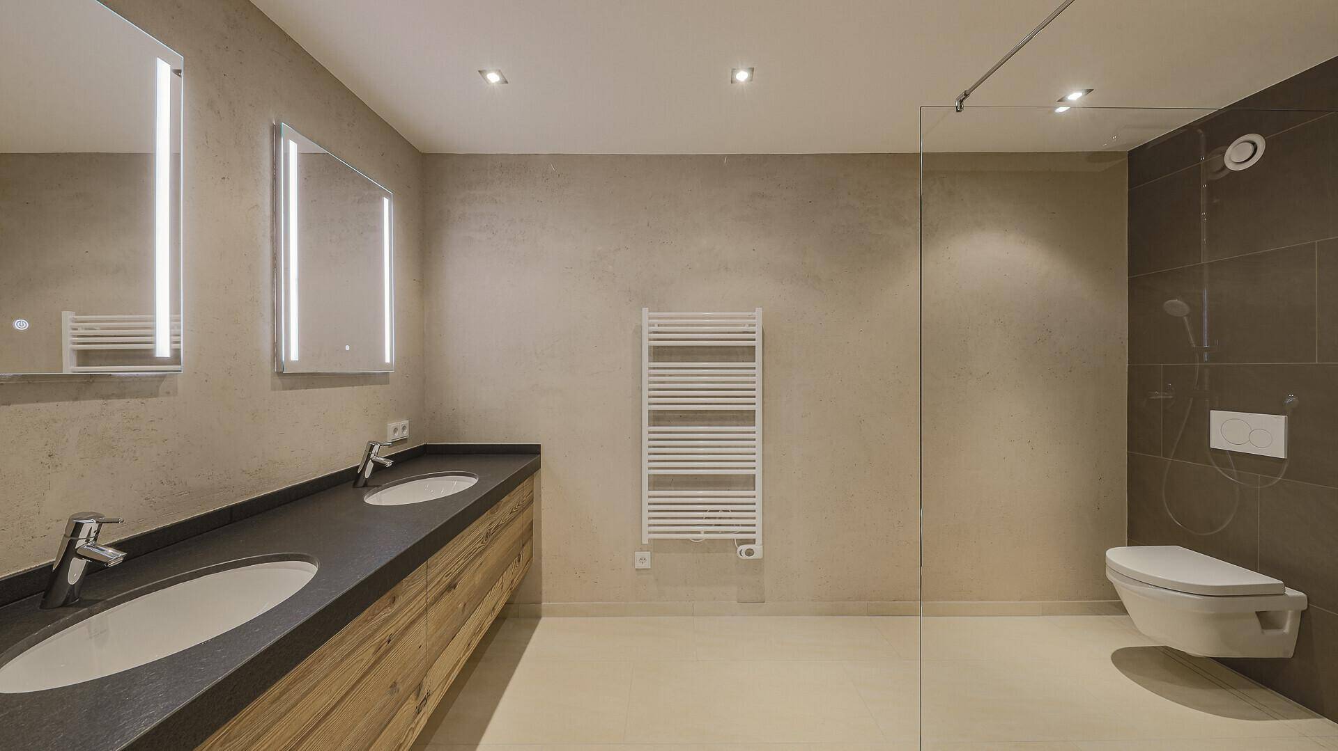 Modernes Badezimmer mit Doppelwaschbecken, wandhängendem WC, begehbarer Dusche und Handtuchheizkörper.