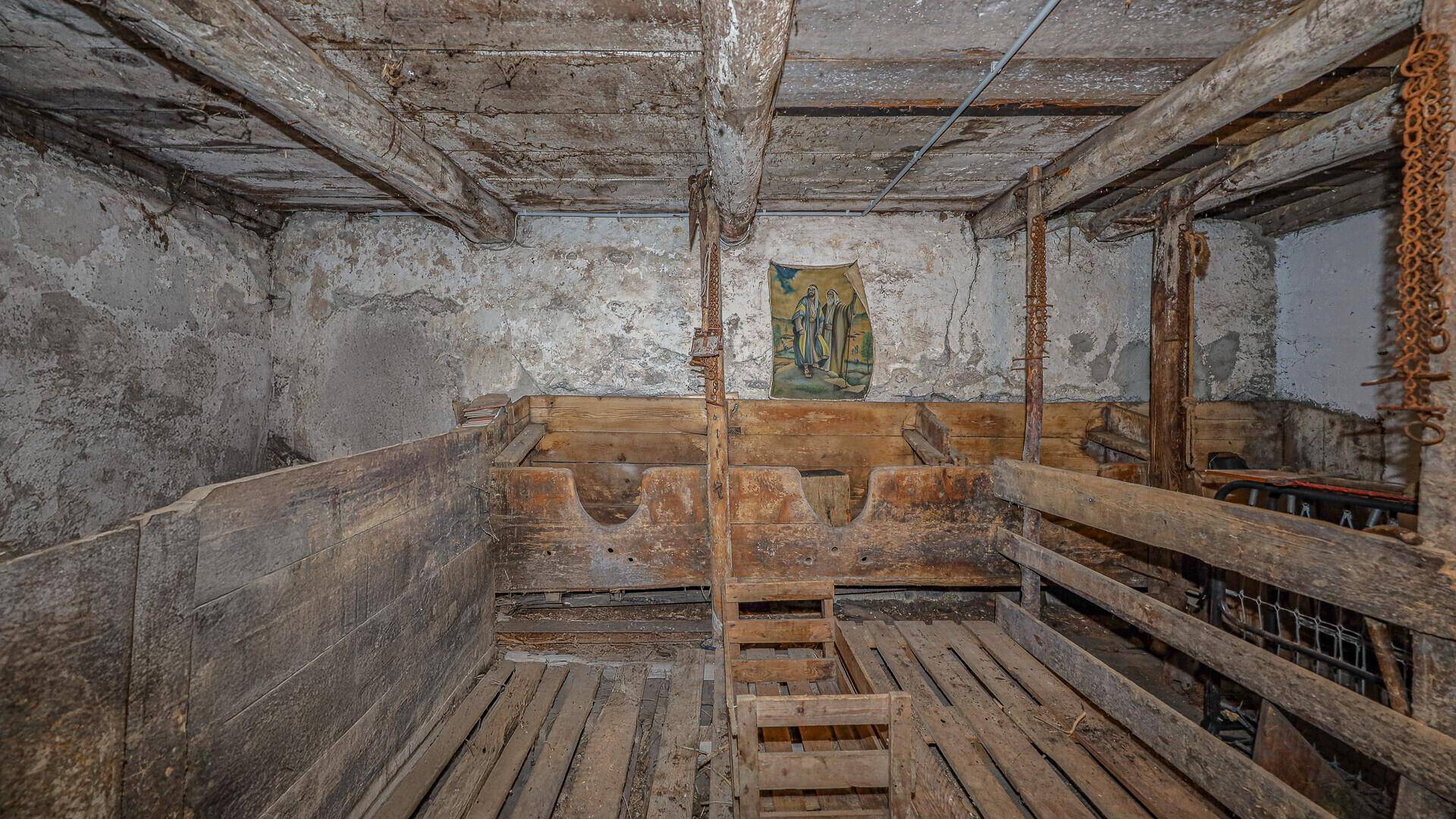 Alter Kellerraum mit rustikalen Holzbalken und rauen Steinwänden, möglicherweise ein ehemaliger Stall.