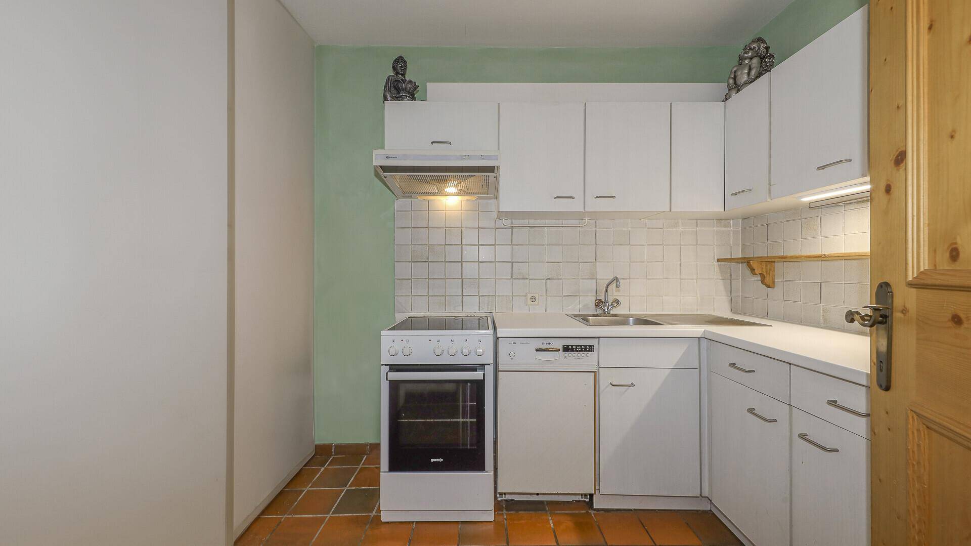 Funktionale Küche mit weißen Schränken, Fliesenboden und grundlegenden Geräten.
