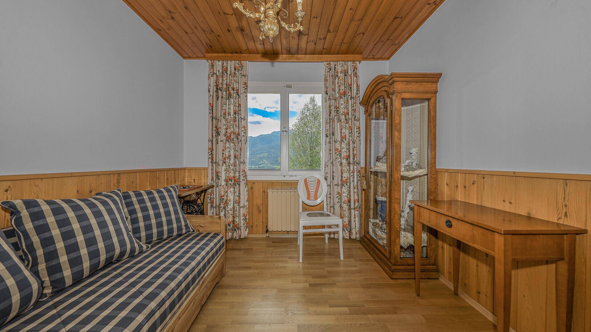 Schlafzimmer mit Holzdecke, Holzvertäfelung und Blick auf die grüne Landschaft.
