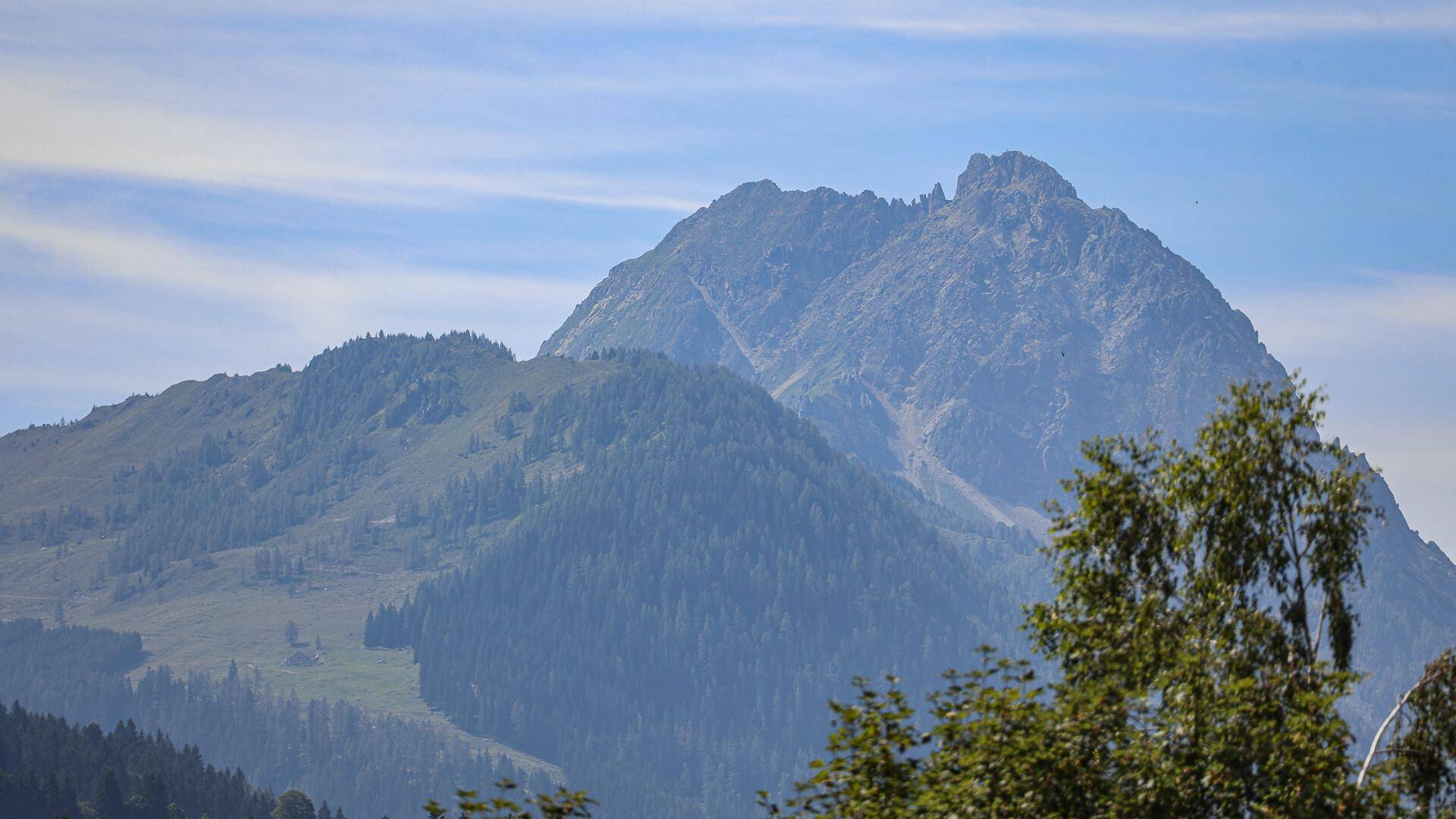 Majestätische Berglandschaft mit bewaldeten Hängen unter einem leicht bewölkten Himmel.