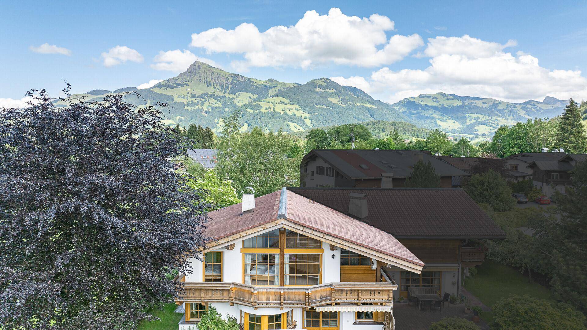 Weitläufiger Ausblick auf das charmante Chalet und die beeindruckende Bergkulisse unter blauem Himmel.
