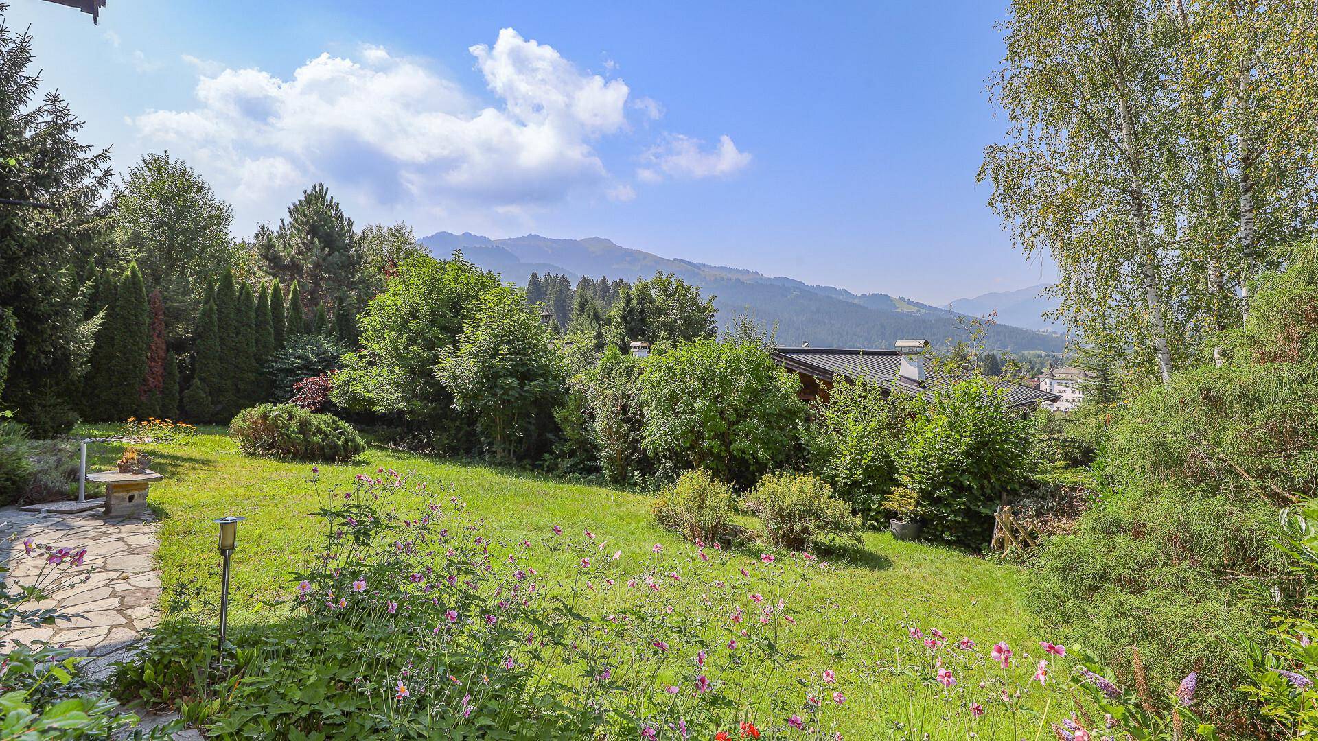 Sonniger Garten mit blühenden Pflanzen und einem malerischen Ausblick auf die Berge.