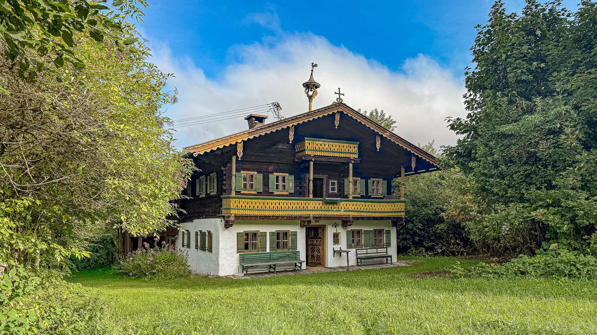 Traditionelles bayerisches Chalet mit Holzbalkonen und Blumenkästen, umgeben von grüner Natur.