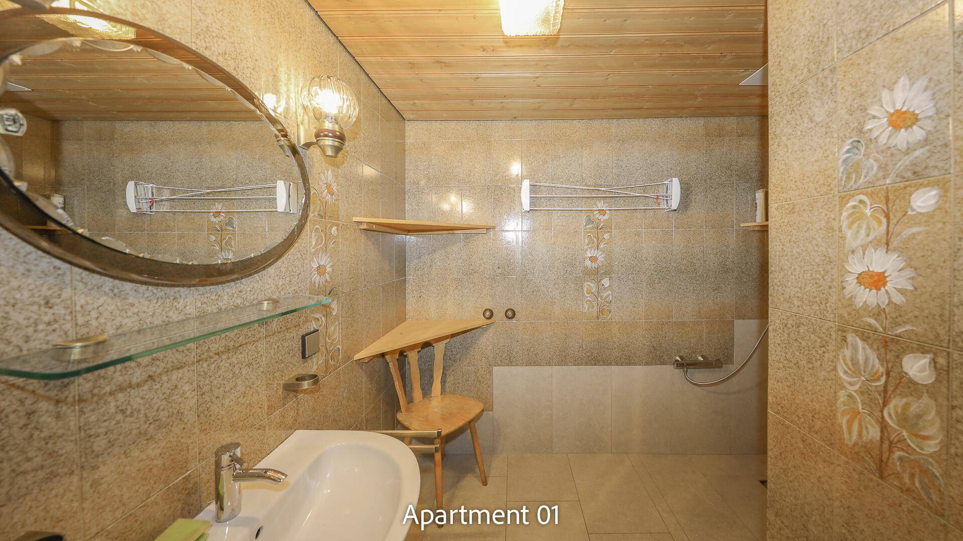 Badezimmer von Apartment 01 mit gemusterten Fliesen, Waschbecken und Duschbereich.