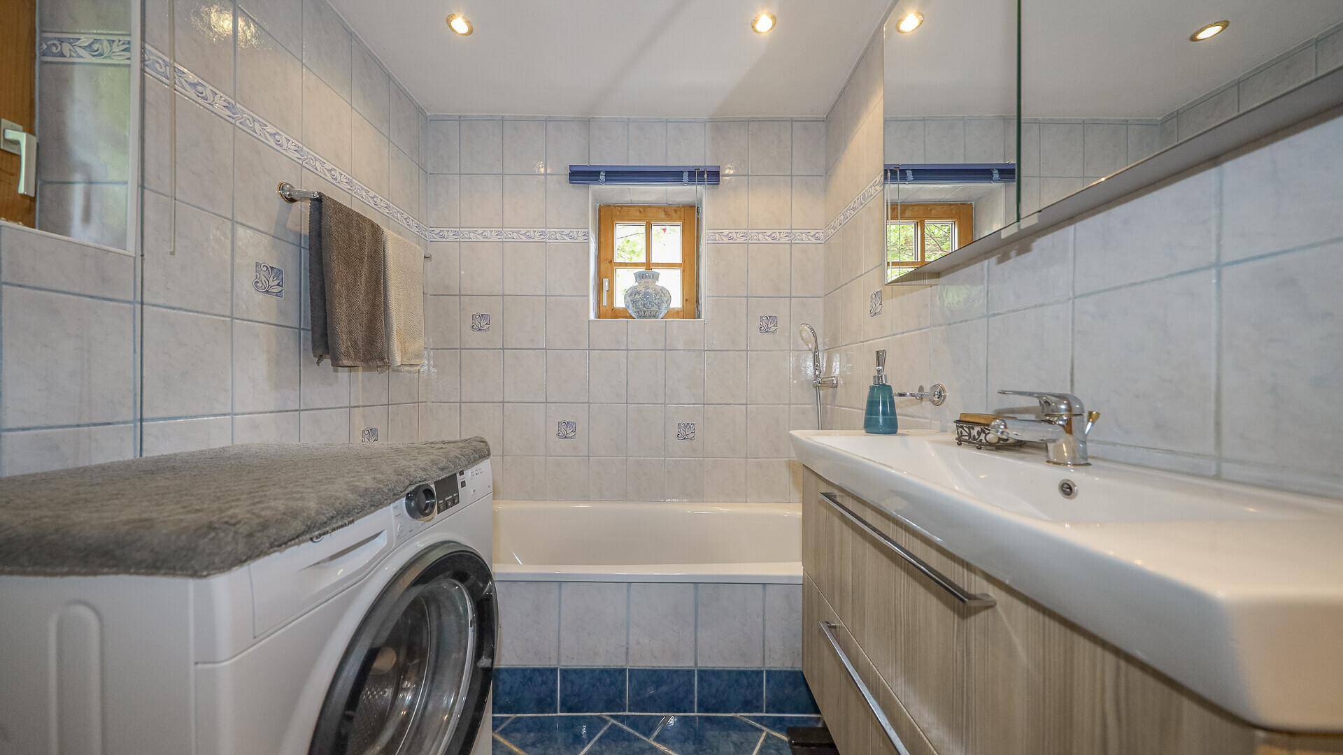 Badezimmer mit Badewanne, Waschbecken und Waschmaschine, gefliest in hellen und blauen Tönen.