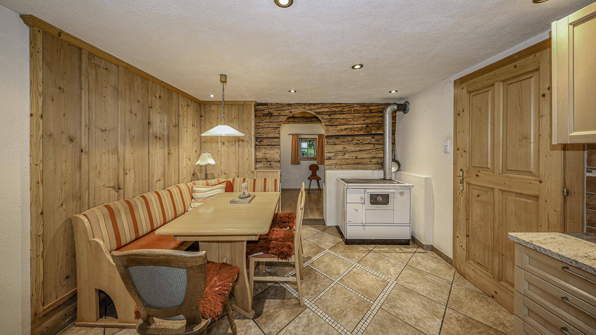 Traditionelle Wohnküche mit Holzbänken, Kachelofen und gefliestem Boden im Landhausstil.