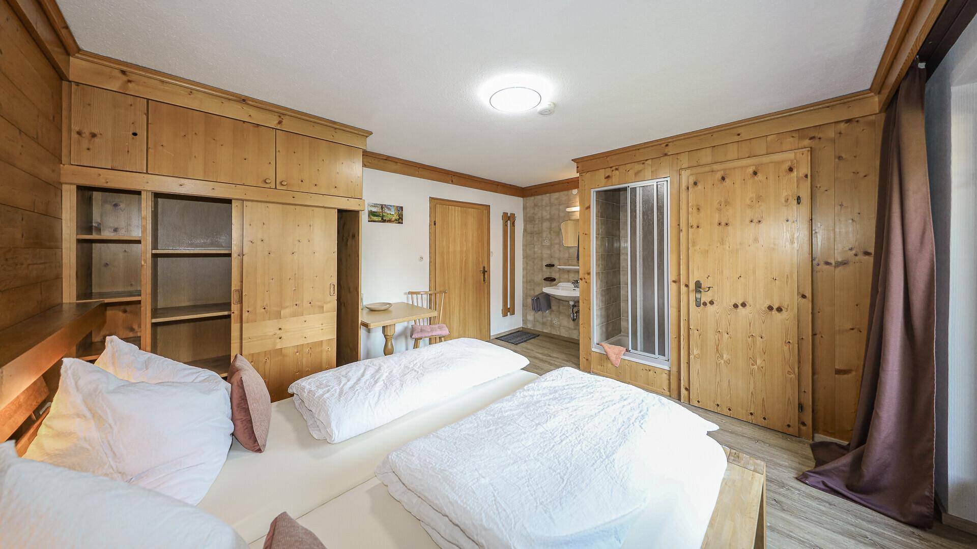 Helles Schlafzimmer mit Holzvertäfelung, Einbauschränken und integriertem Duschbereich.