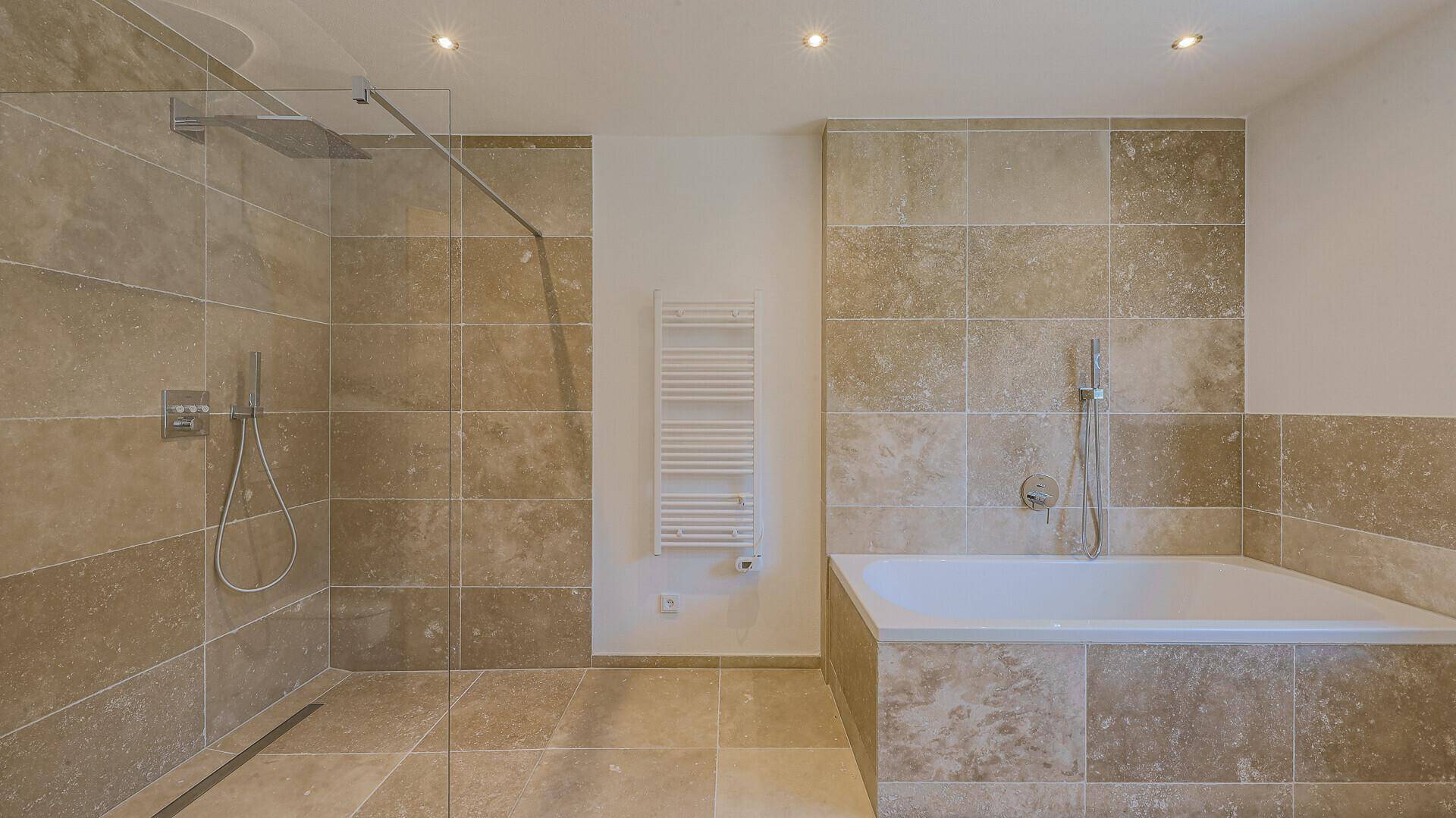 Modernes Badezimmer mit begehbarer Dusche, Badewanne und beigefarbenen Fliesen, ausgestattet mit Handtuchheizkörper.